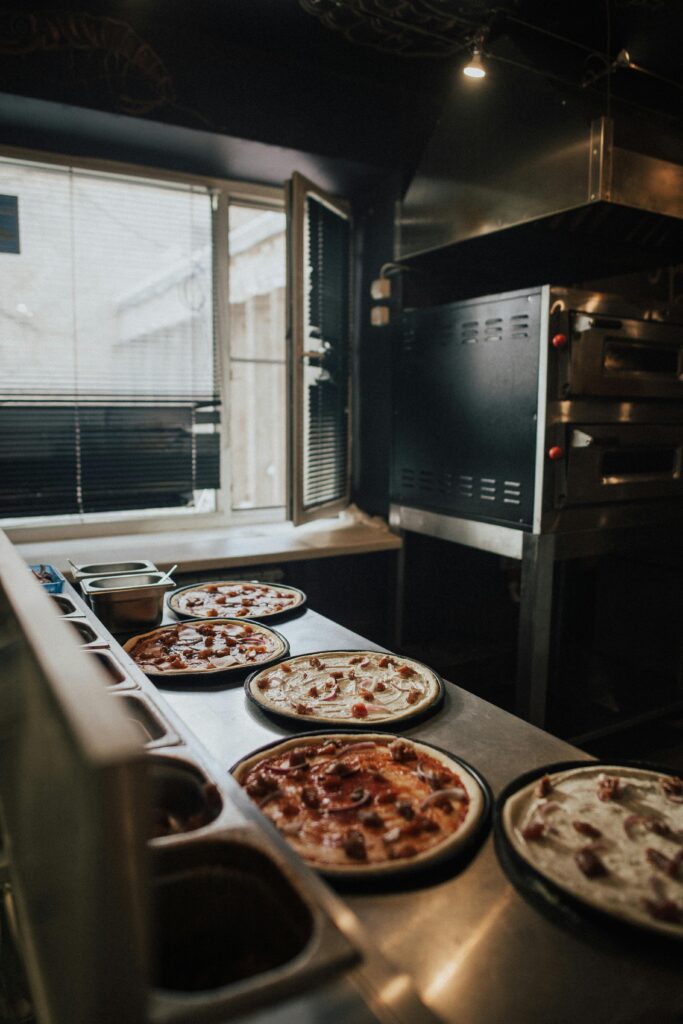 A selection of pizzas prepared in an indoor kitchen near a window, highlighting the cooking atmosphere.